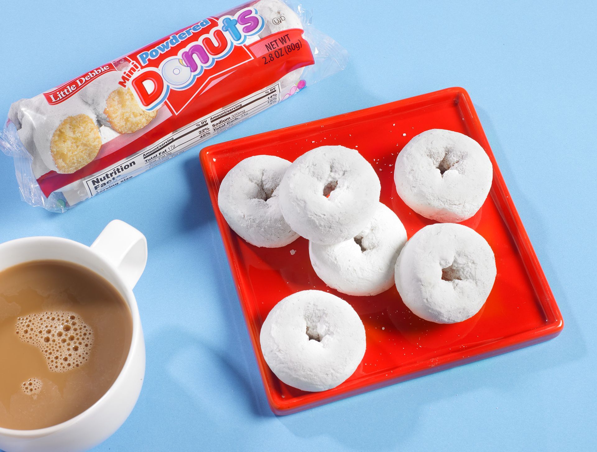 a group of powdered mini donuts on a red plate sitting on top of a blue background with a cup of coffee
