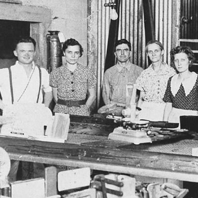 A black and white photo of a group of people standing around a table