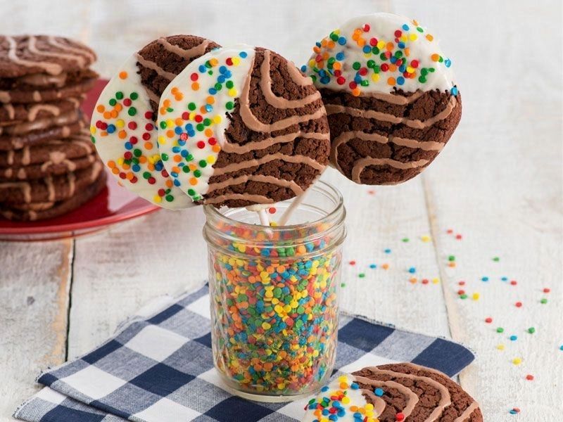 A jar filled with chocolate cookies and sprinkles on sticks.