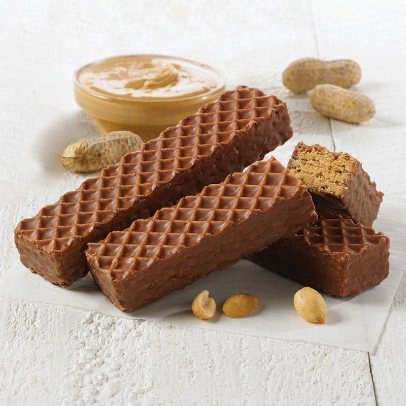 three nutty buddy wafer bars sitting on a wooden board with peanut butter and peanuts around 