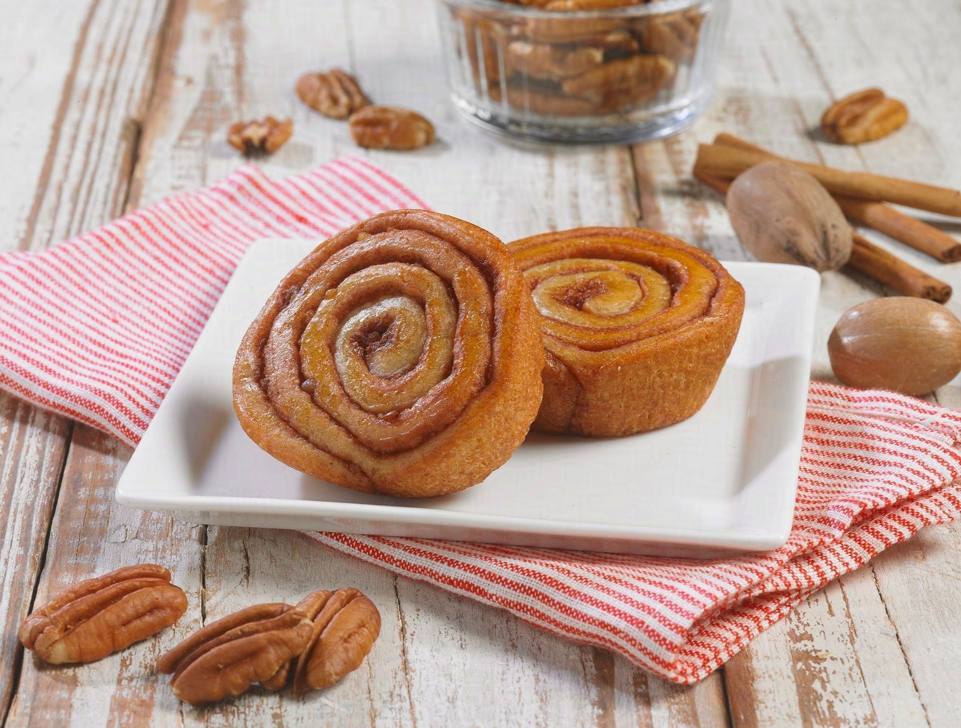 A white plate topped with two cinnamon rolls and pecans