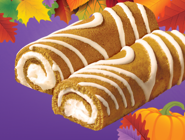 Two pumpkin rolls with white frosting and a slice of pumpkin pie in the background