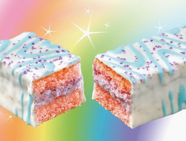 Two pieces of cake with blue frosting and sprinkles on a rainbow background