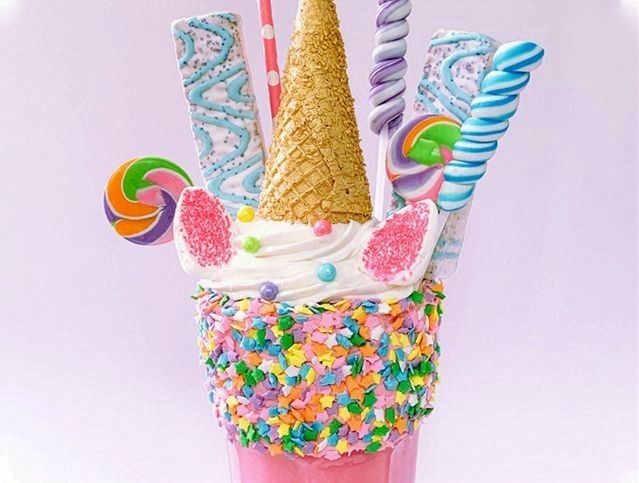 A milkshake decorated to look like a unicorn with ice cream cones , lollipops , and sprinkles.