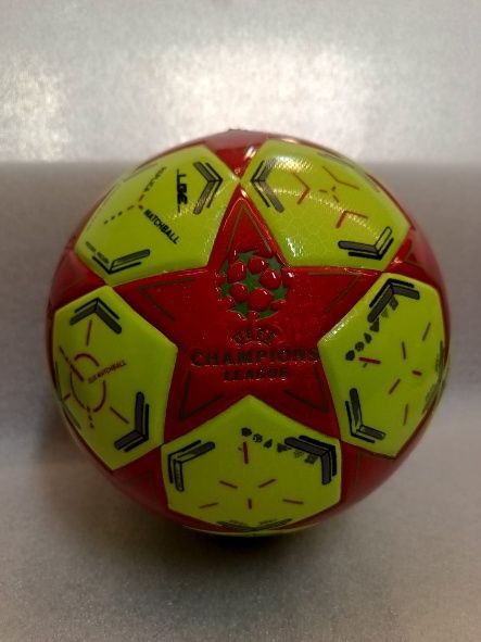 Balón de fútbol rojo y amarillo sobre una superficie gris claro.
