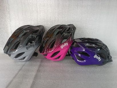 Tres cascos de bicicleta de color gris, rosa y morado, dispuestos uno al lado del otro sobre una superficie clara.