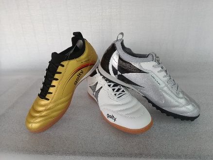 Tres botas de fútbol: una dorada y negra, dos blancas y negras sobre una superficie gris.