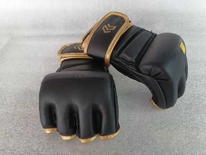 Un par de guantes de boxeo negros con ribetes y correas doradas sobre un fondo gris.