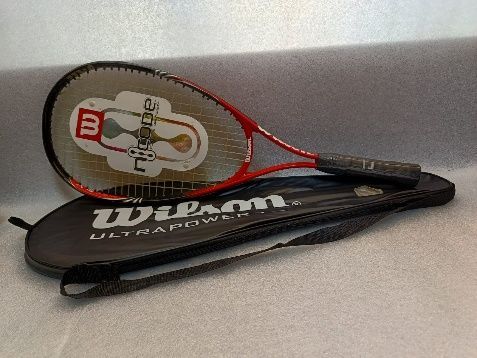 Una raqueta de tenis Wilson descansa sobre un estuche negro de la misma marca, con otra raqueta con marco rojo detrás.