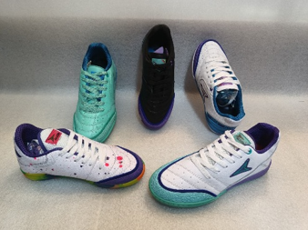 Cinco zapatillas deportivas de color verde azulado, blanco, negro y morado dispuestas en círculo sobre una superficie gris.