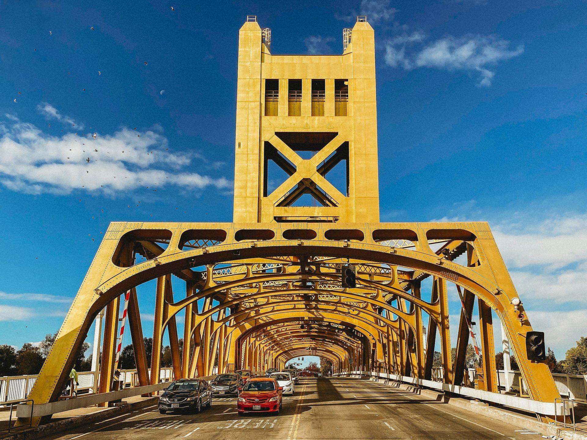 Yellow Tower Bridge with cars on the road under a blue sky.