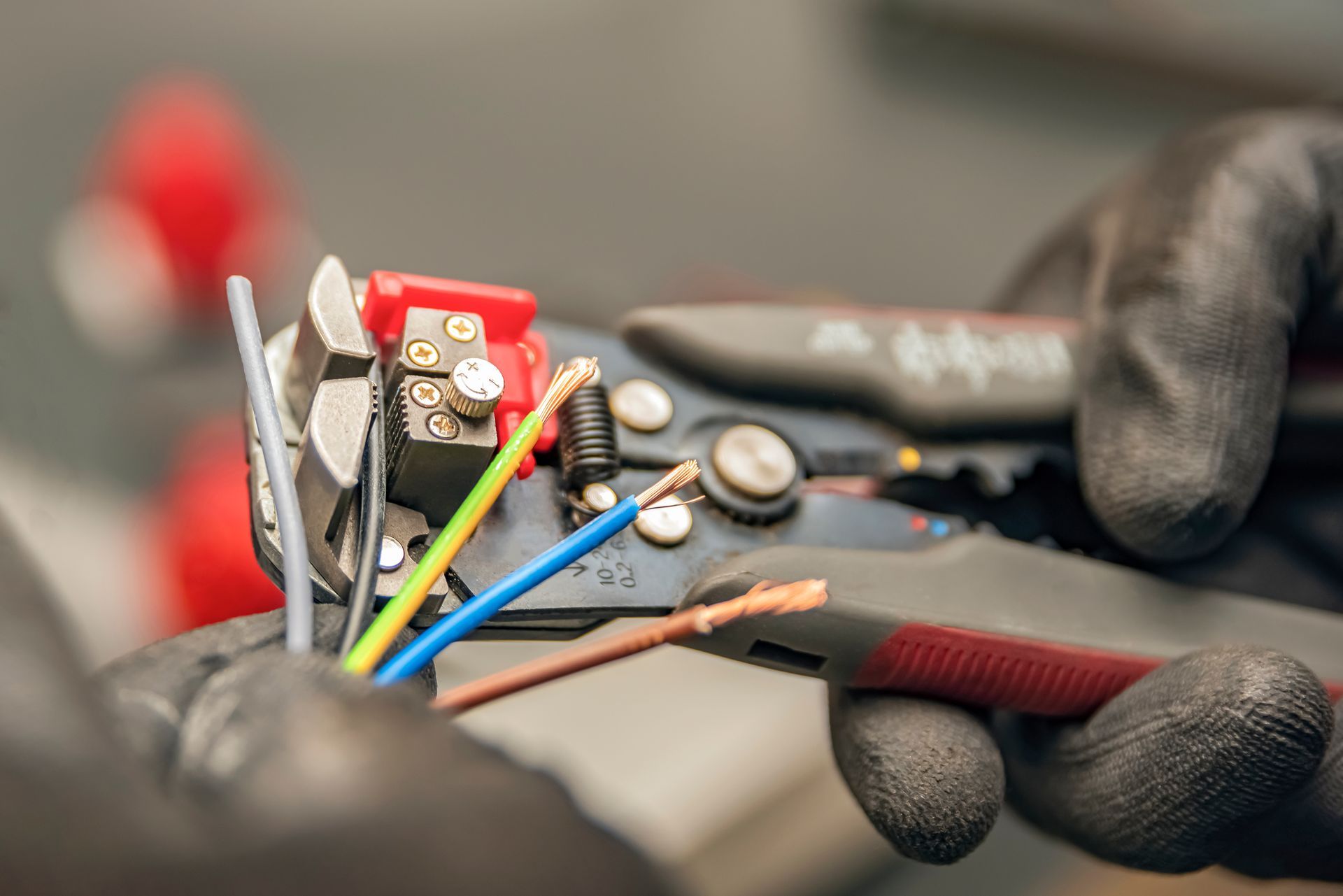 Close-up of wire stripper tool cutting colored electrical wires.