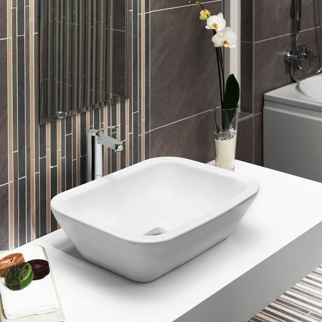 Modern bathroom sink with white vessel basin on a vanity beside gray tile and a white orchid