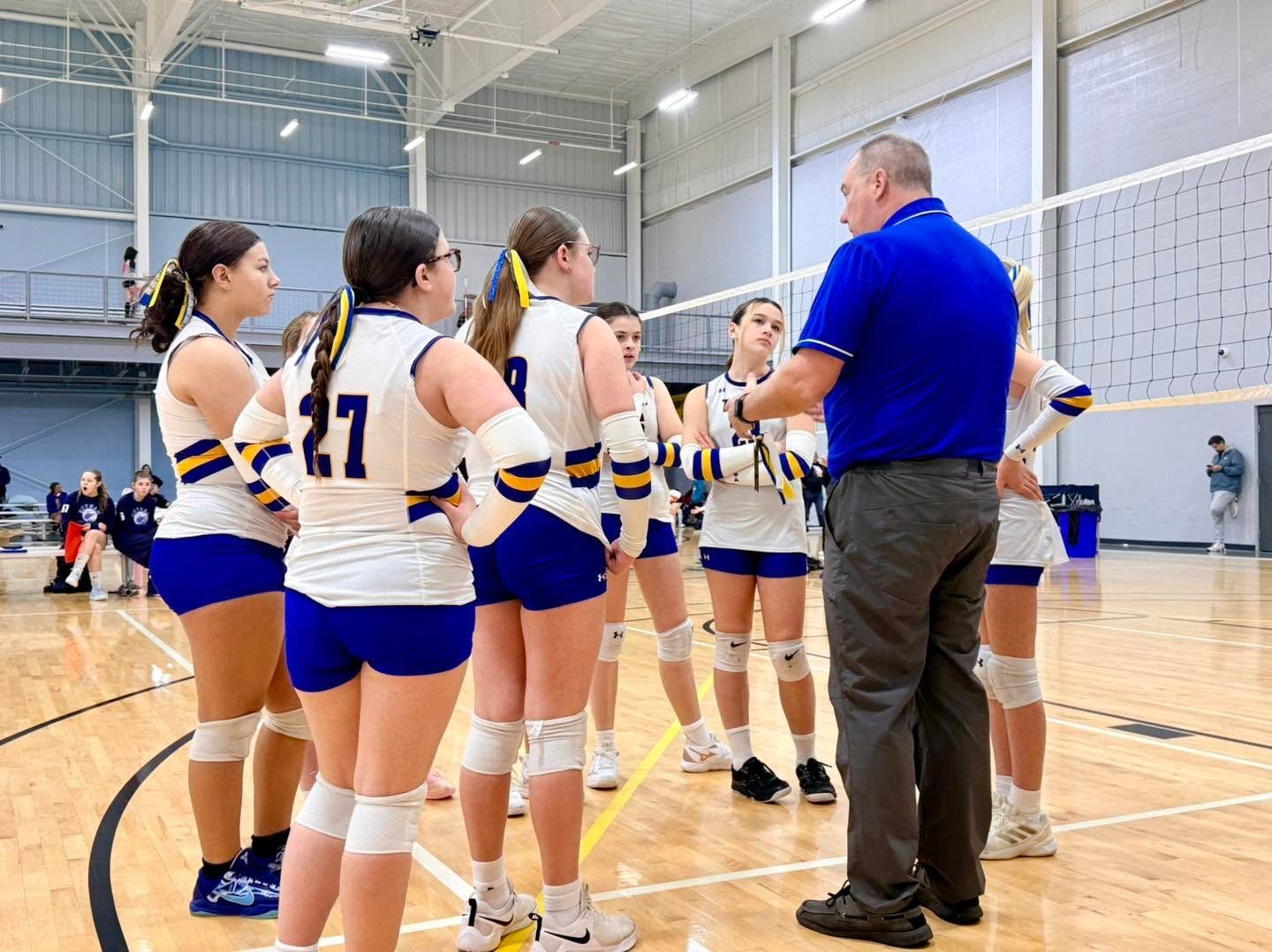 Volleyball team huddles with coach on indoor court during a game timeout