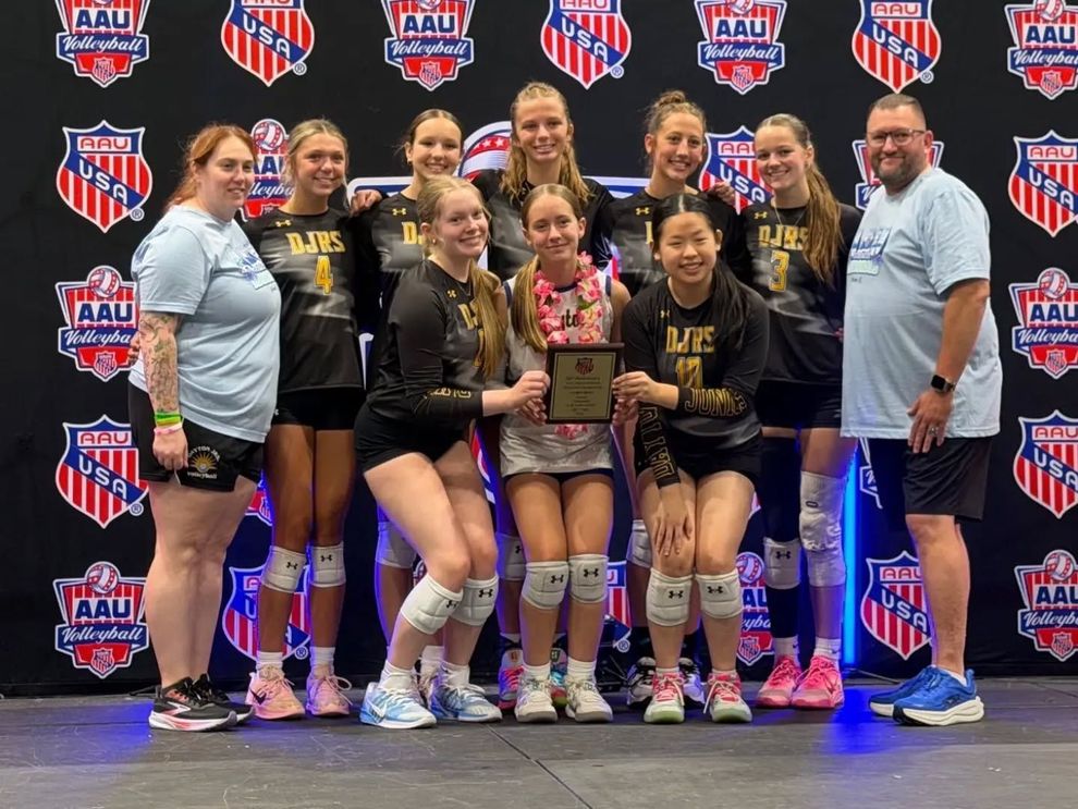 Youth volleyball team posing with trophy at AAU event backdrop