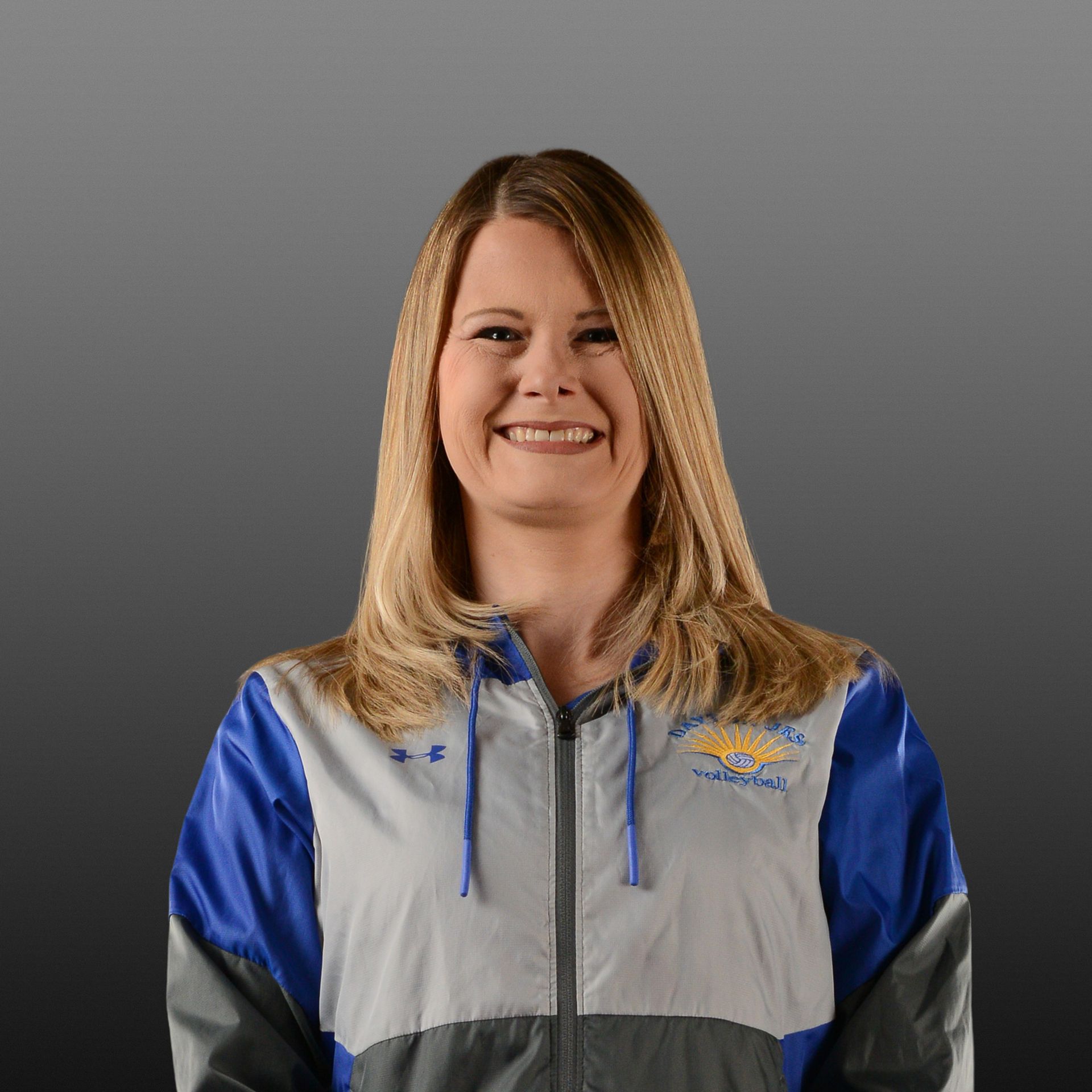 Smiling person in a blue and gray zip-up jacket against a gray background