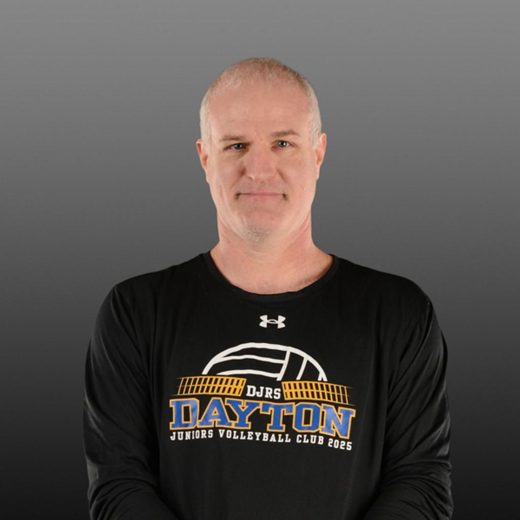 Man in black Dayton volleyball T-shirt, smiling against a gray background