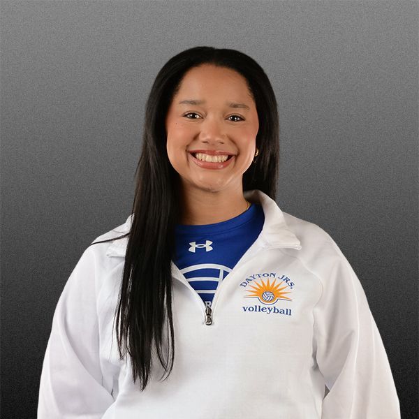 Smiling person in a white jacket with a blue volleyball shirt against a gray background