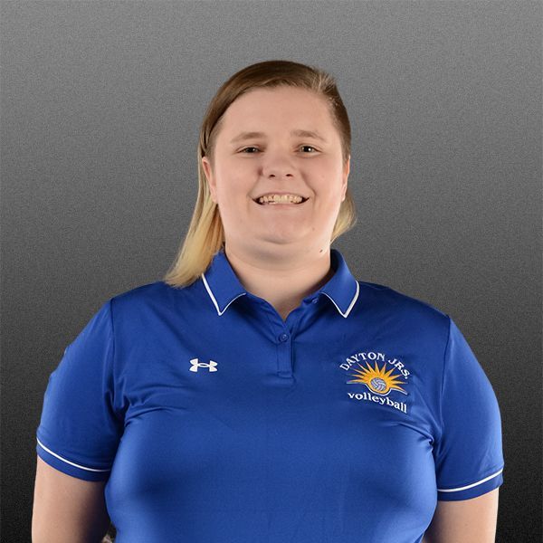 Person in a blue polo shirt smiling against a gray background