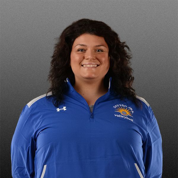 Smiling person in a blue zip-up athletic top against a gray backdrop