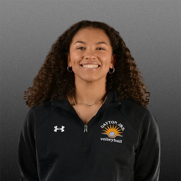 Portrait of a smiling person in a black Dayton volleyball jacket on a gray background