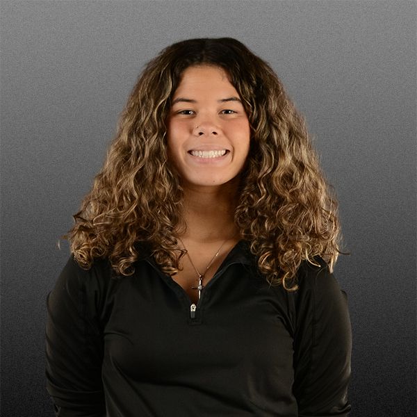 Smiling person with curly brown hair wearing a black top against a gray background