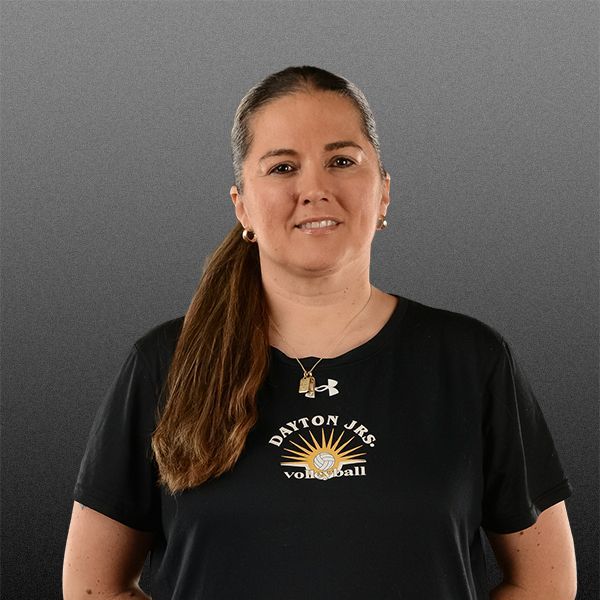 Woman in black Dayton Junior Volleyball shirt smiling against a gray background