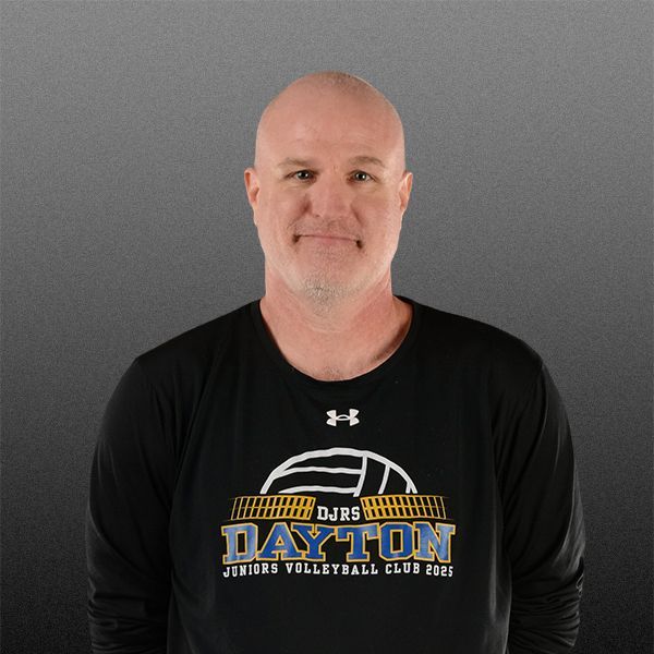 Man in black long-sleeve shirt with Dayton volleyball club logo, standing against a gray background