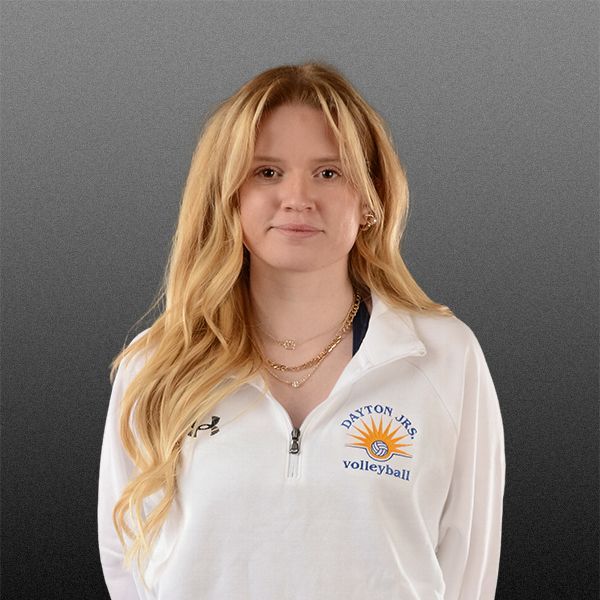 Young woman in a white jacket with a volleyball logo, standing against a gray background.