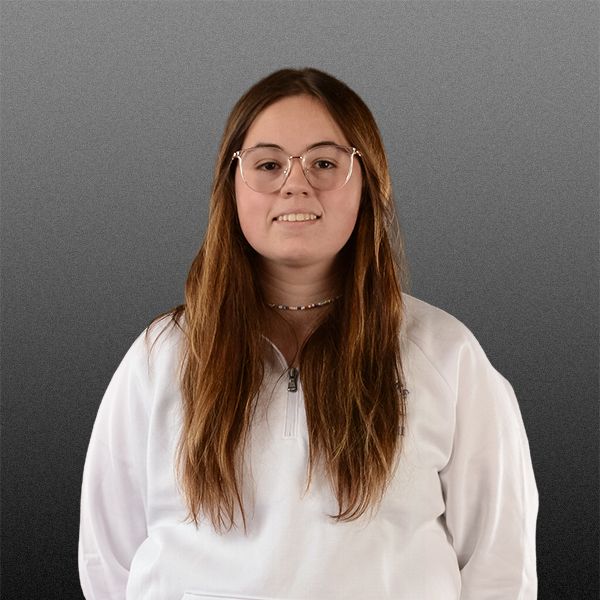 Portrait of a person with long brown hair, glasses, and a white shirt against a gray background