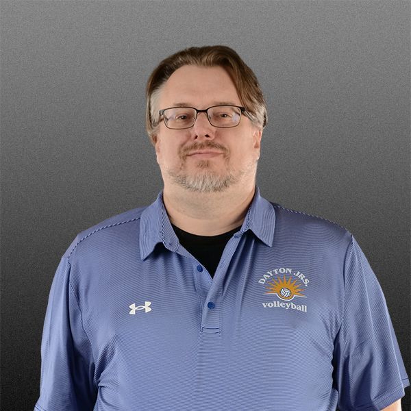 Man in glasses wearing a blue polo shirt against a gray background