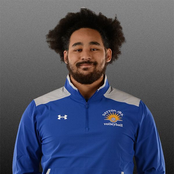 Smiling person in a blue athletic jacket against a gray studio background