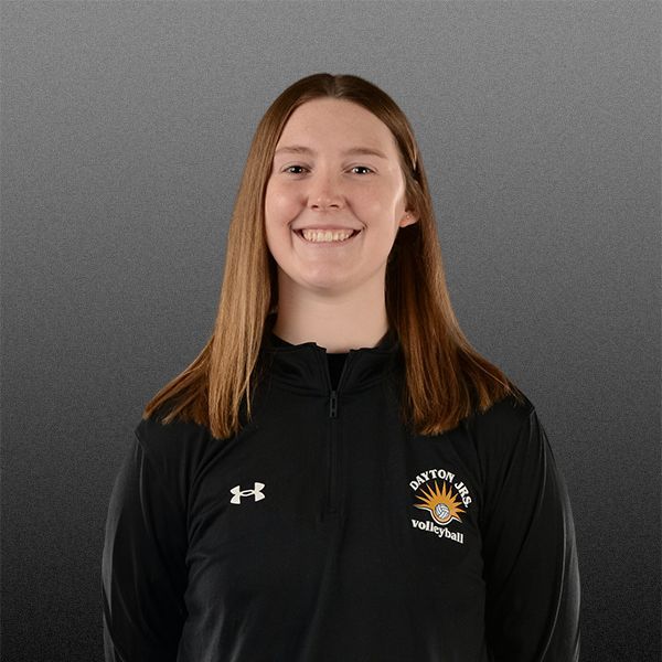 Smiling person in a black jacket against a gray background with a sports team logo