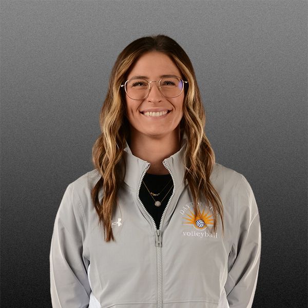 Smiling person in glasses and a gray zip-up jacket against a plain gray background