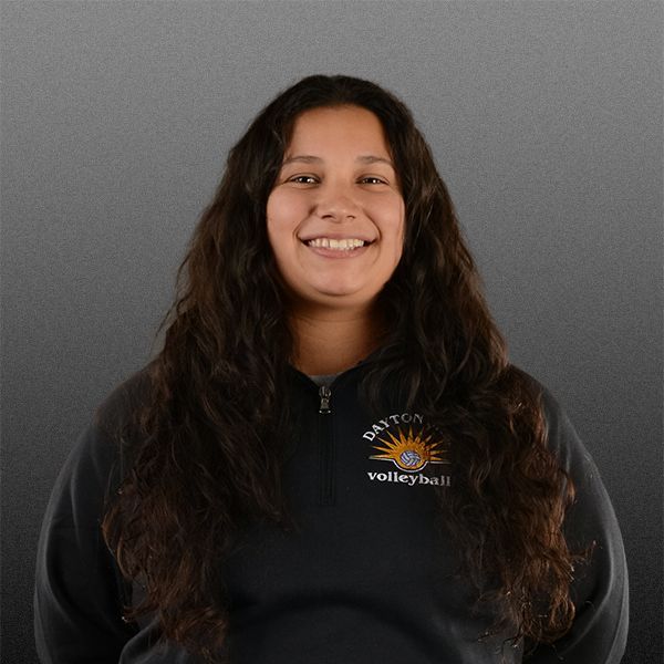 Smiling person with long dark hair in a black sweatshirt against a gray background