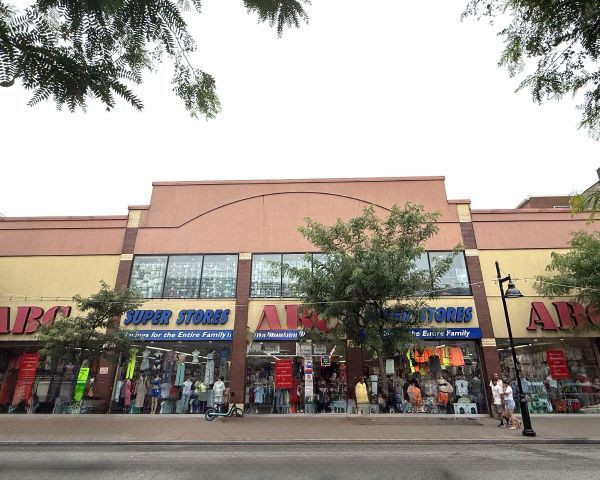 Exterior view of ABC Super Store; building with large windows, clothing on display, people walking in front.