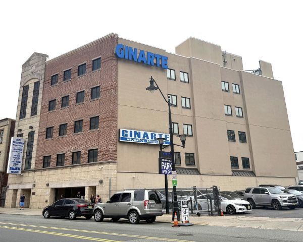 A brick and beige building with the Rinarta sign; cars parked in front.