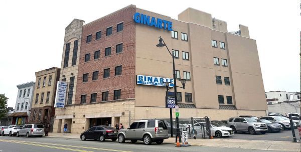 A brick and beige building with the Rinarta sign; cars parked in front.