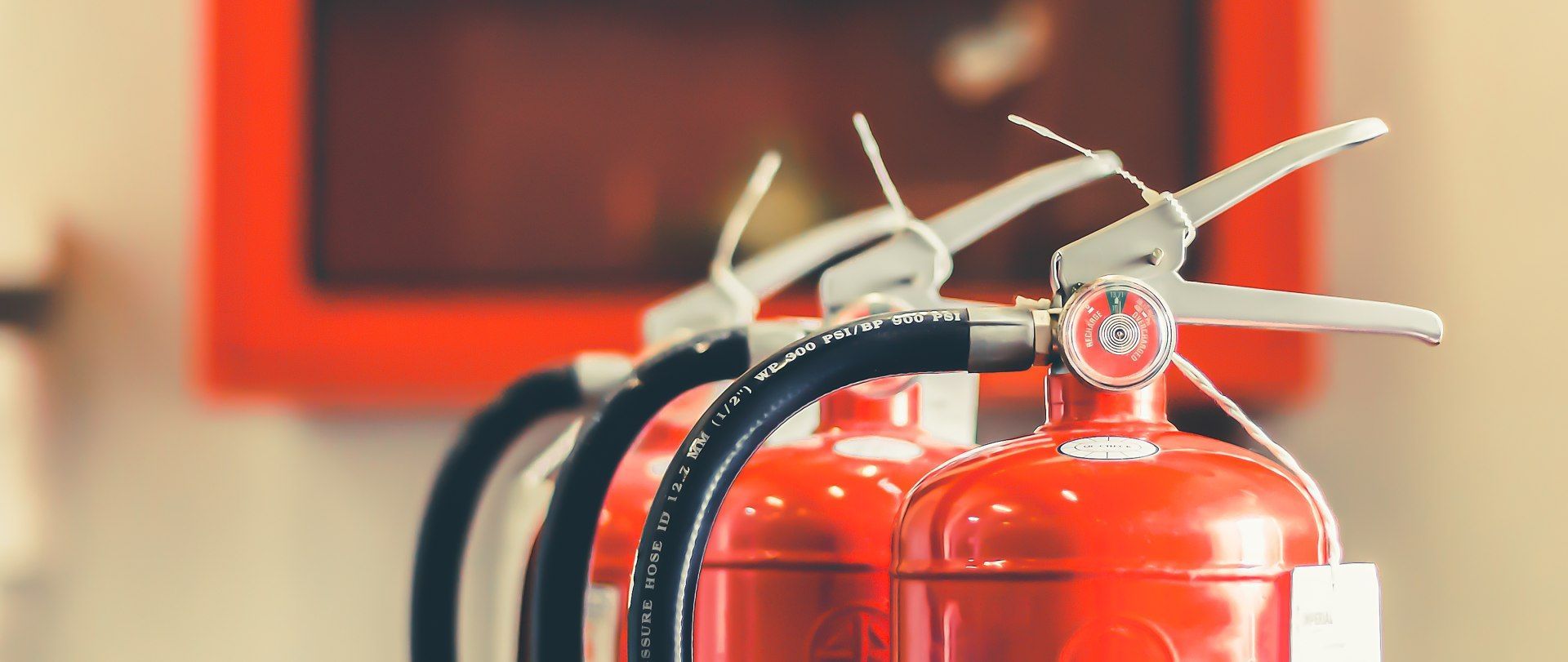 Row of red fire extinguishers with silver handles on a wall.