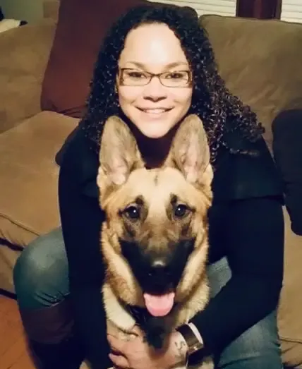 Woman sitting on a couch with a German Shepherd, both facing the camera and smiling