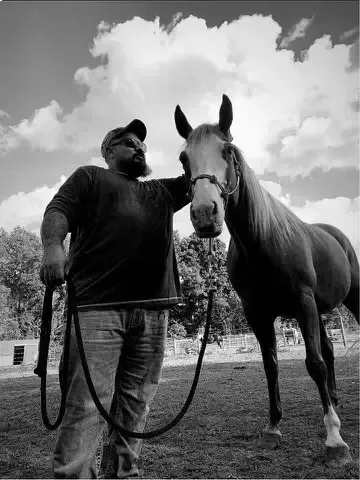 Person standing with a horse on a leash in a grassy field under cloudy sky