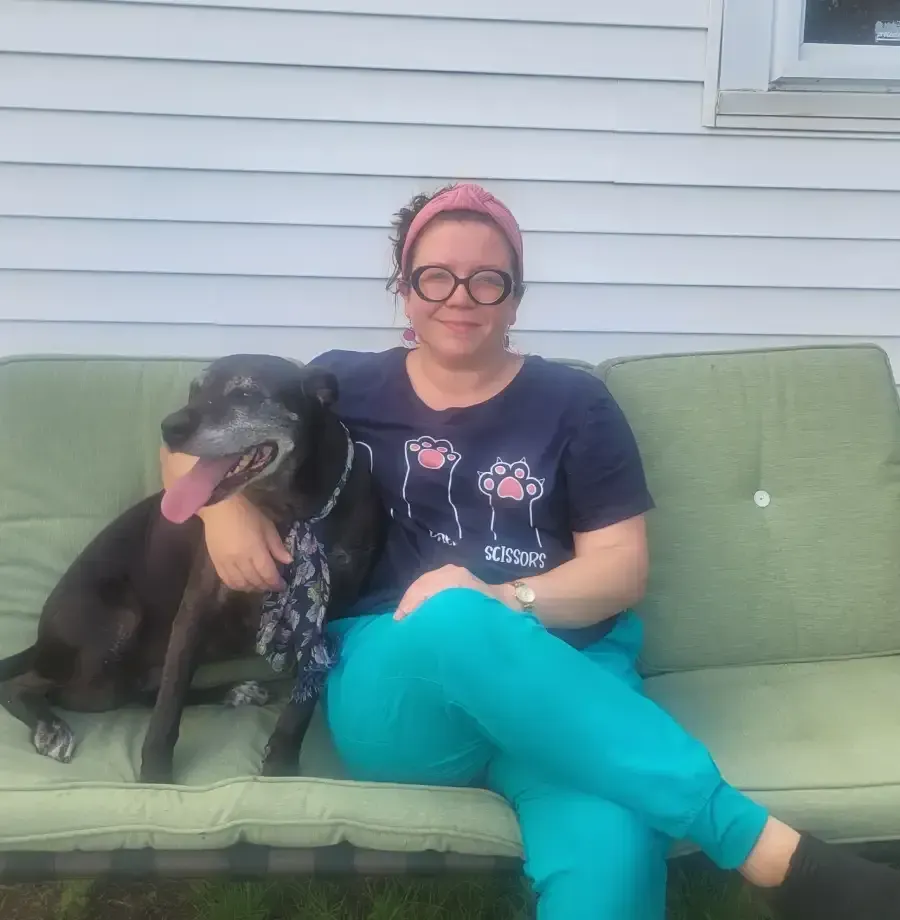 Person sitting on a green outdoor couch with a black dog, both wearing bandanas.