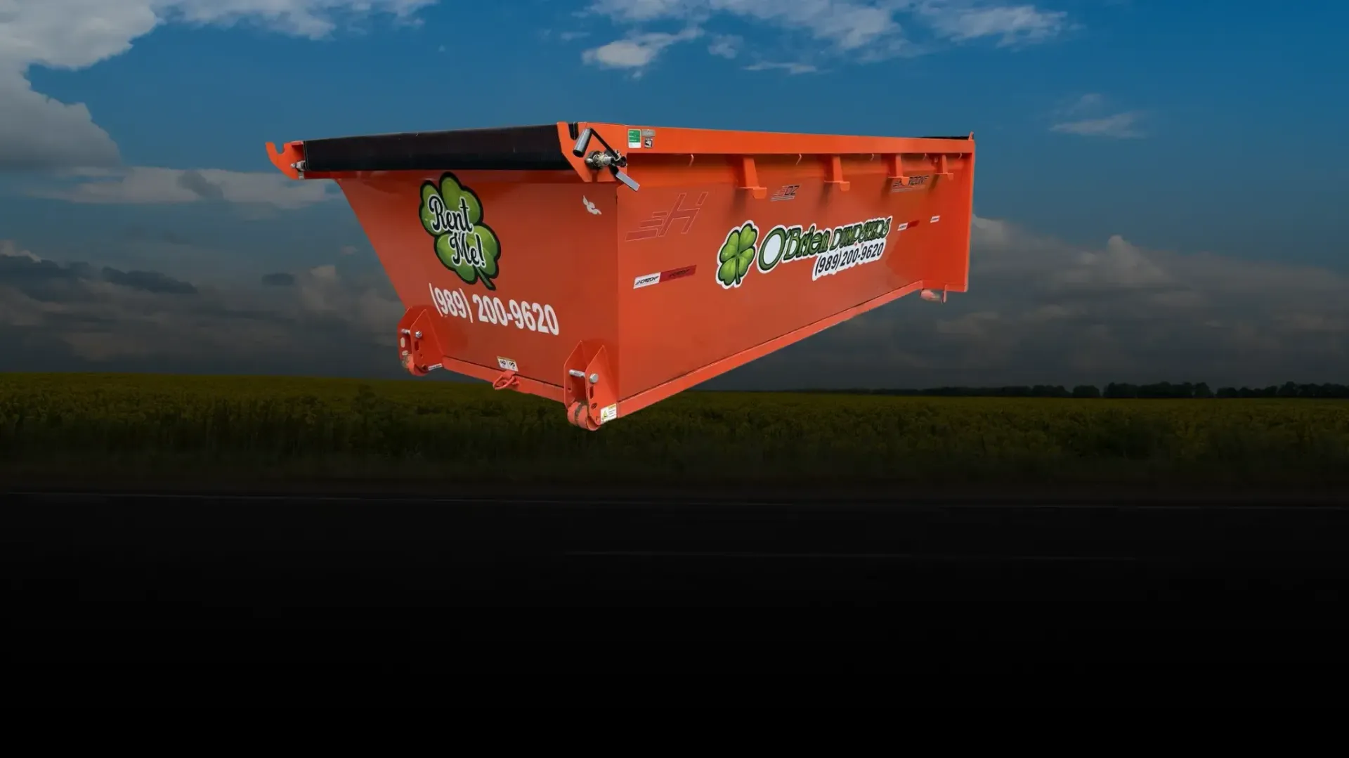 Orange dumpster with graffiti floating above a dark landscape at sunset