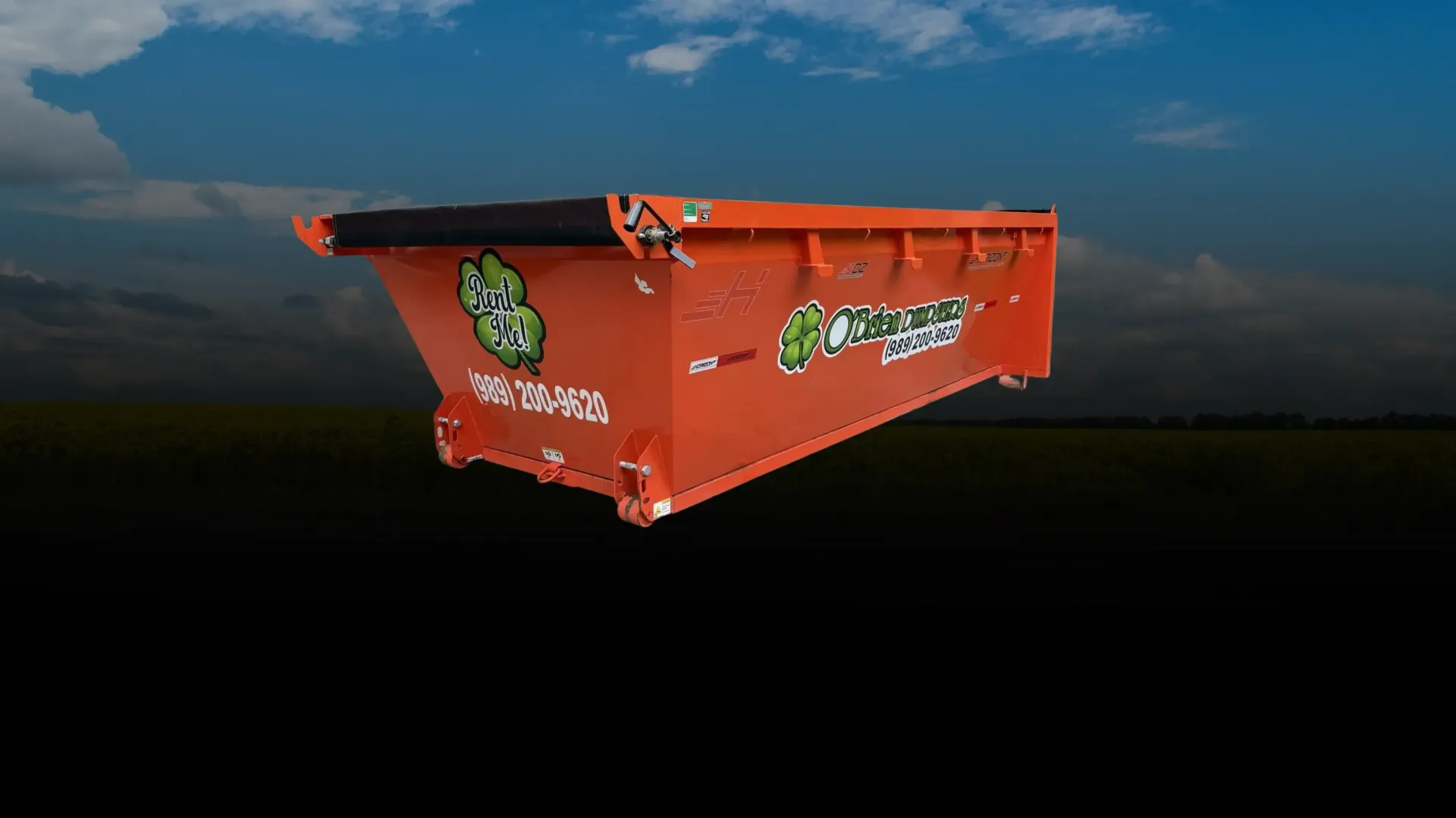 Orange dumpster with green logo on a dark roadside under a cloudy sky