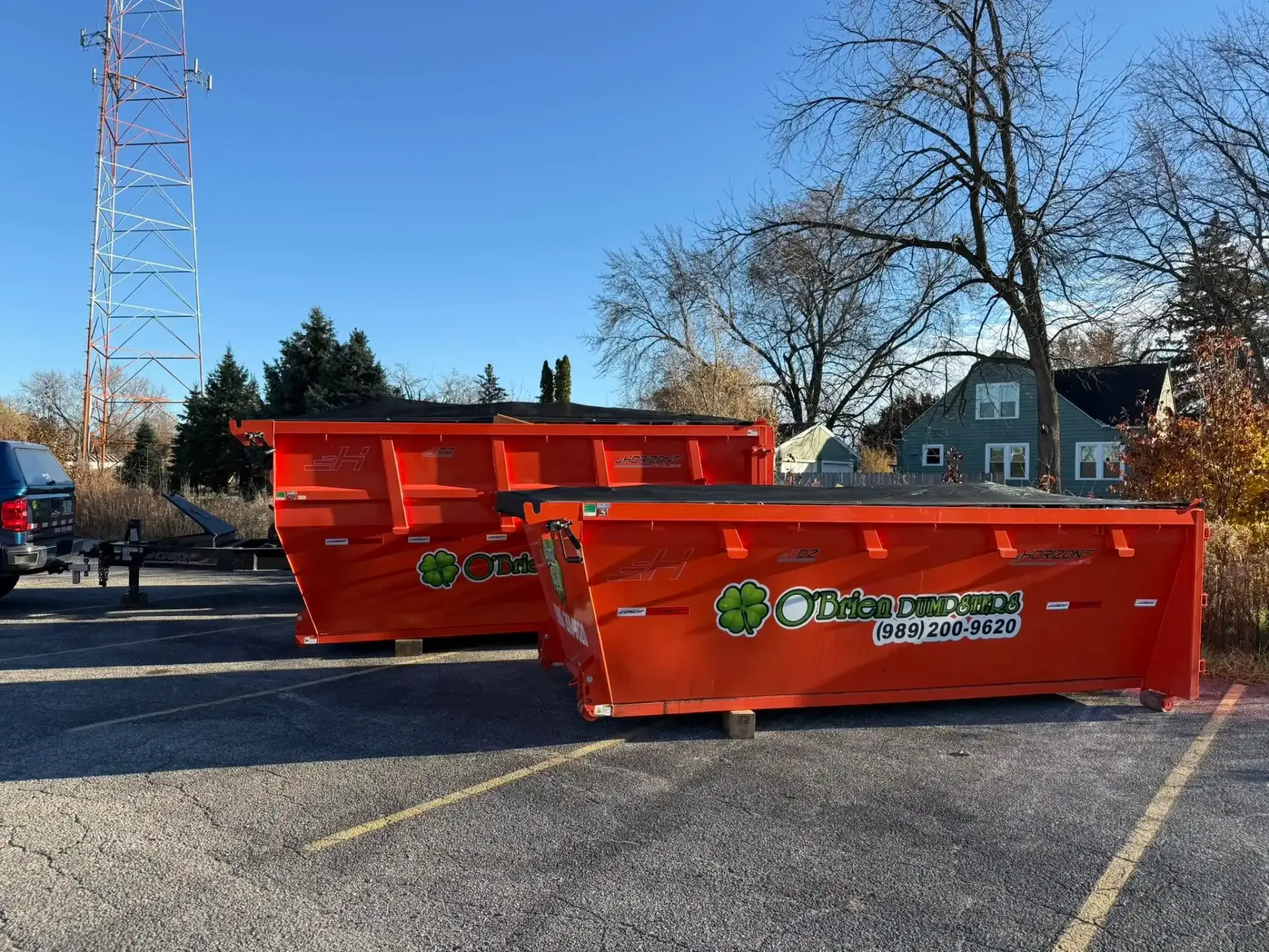 Two orange dumpsters in a parking lot under a clear blue sky.