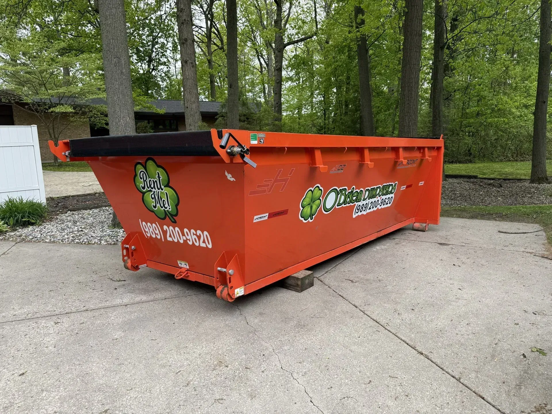 Orange dumpster with graffiti on a concrete driveway in a wooded area
