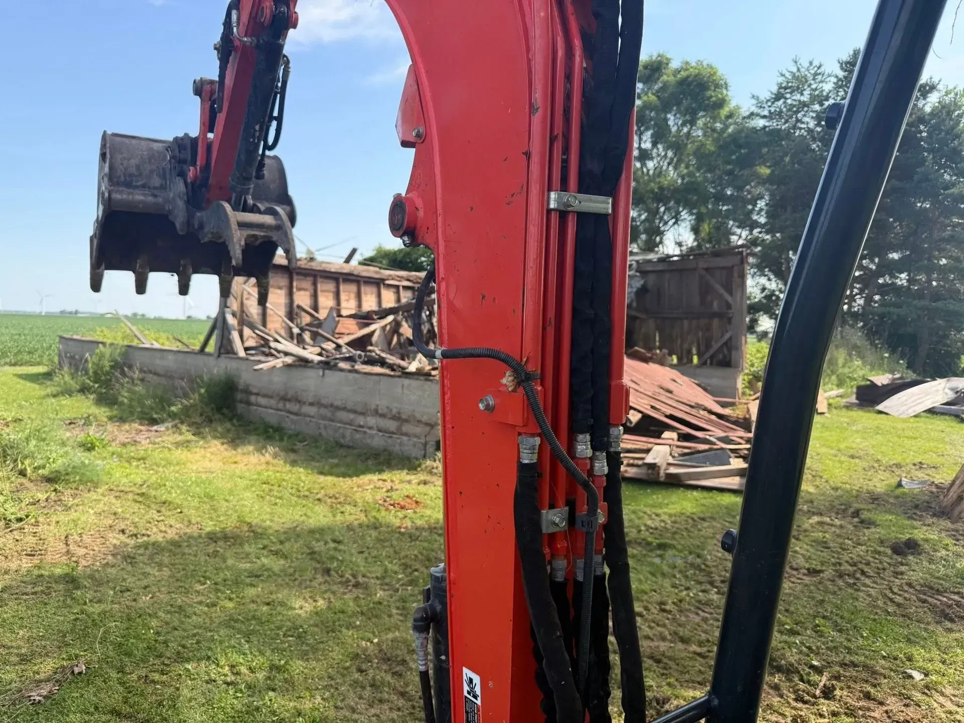 Red excavator arm with bucket beside a pile of debris in a grassy field under a cloudy sky