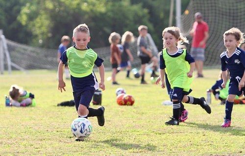 Children playing soccer on a grassy field, two in neon green jerseys chasing the ball.