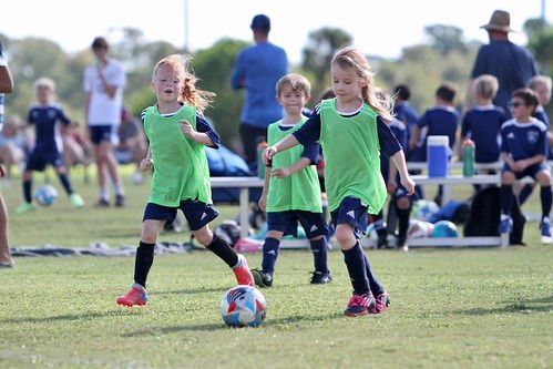 Children in green jerseys playing soccer on a grassy field during a youth game