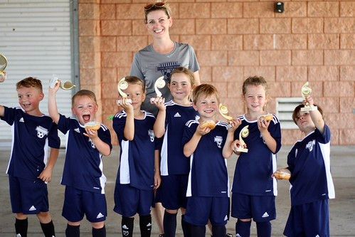 Group of children in navy sports uniforms holding trophies with an adult standing behind them outdoors